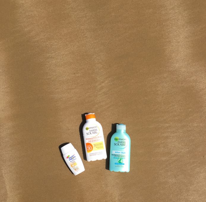 Am Strand in Spanien. Die Sonnenmilch von Garnier Ambre Solaire liegt im Sand.